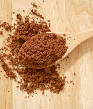 Cocoa powder in wooden spoon spilling on table