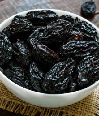 Prunes in a ceramic bowl on a dark wooden background. Dried fruits.